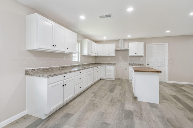 918 N Gray St, Amarillo, TX 79065 - kitchen featuring butcher block countertops, wall chimney range hood, light wood finished floors, white cabinetry, and recessed lighting