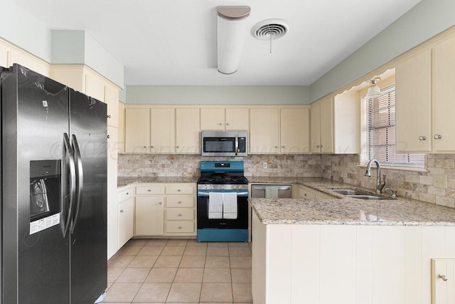 5003 Greenway Pl, Amarillo, TX 79109 - kitchen with appliances with stainless steel finishes, cream cabinetry, a peninsula, tasteful backsplash, and light tile patterned floors