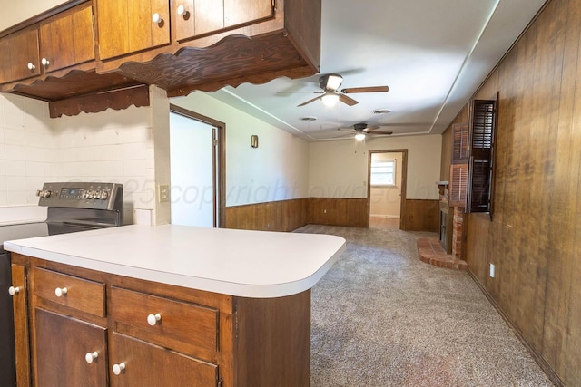 kitchen with electric stove, ceiling fan, carpet flooring, wooden walls, and light countertops