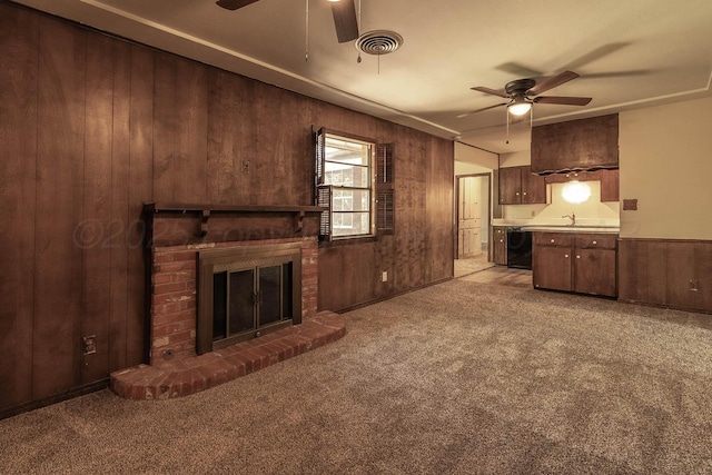 unfurnished living room featuring a ceiling fan, wood walls, carpet floors, a brick fireplace, and a sink