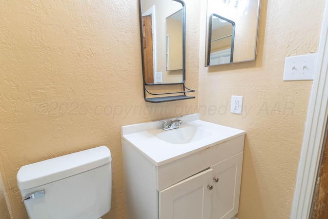 bathroom featuring toilet, vanity, and a textured wall