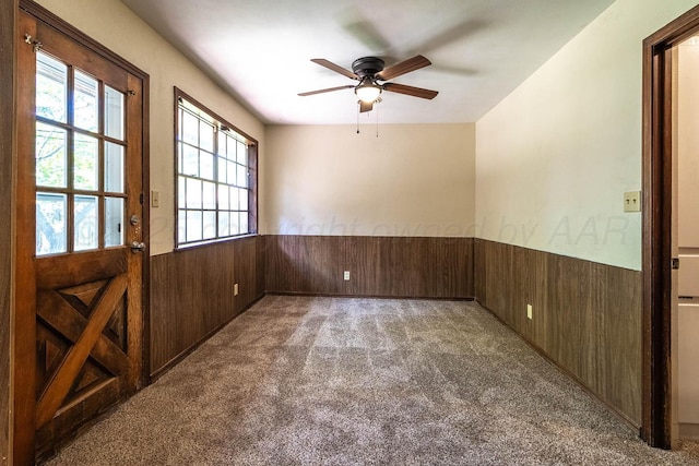 spare room featuring wainscoting, wood walls, carpet, and a ceiling fan