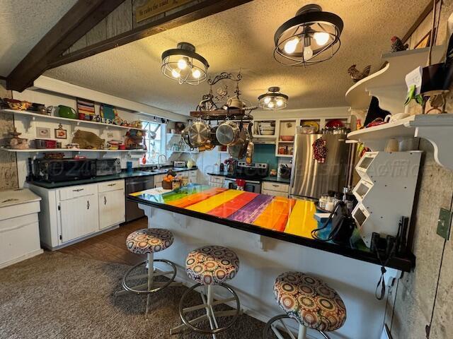 kitchen with white cabinetry, appliances with stainless steel finishes, a textured ceiling, sink, and beamed ceiling