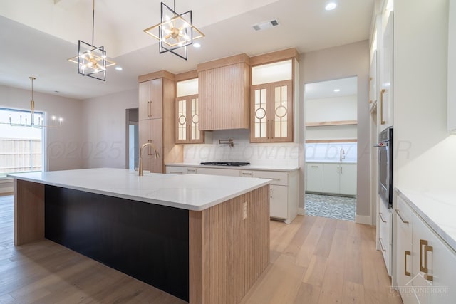 1207 Herring Ranch Rd, Amarillo, TX 79124 - kitchen with a chandelier, light wood-type flooring, backsplash, an island with sink, and appliances with stainless steel finishes