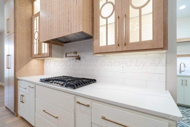 1207 Herring Ranch Rd, Amarillo, TX 79124 - kitchen with stainless steel gas cooktop, extractor fan, backsplash, glass insert cabinets, and light stone countertops