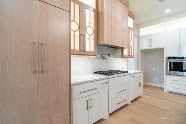 1207 Herring Ranch Rd, Amarillo, TX 79124 - kitchen with stainless steel appliances, decorative backsplash, glass insert cabinets, light wood-type flooring, and white cabinets