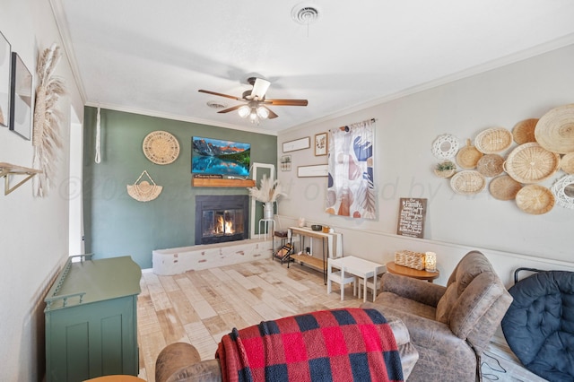 living area featuring crown molding, a glass covered fireplace, ceiling fan, and wood finished floors