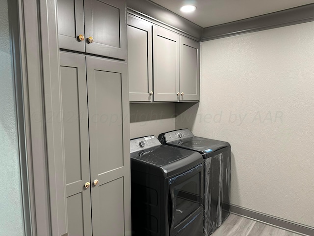 washroom with cabinets, washing machine and clothes dryer, and light hardwood / wood-style flooring