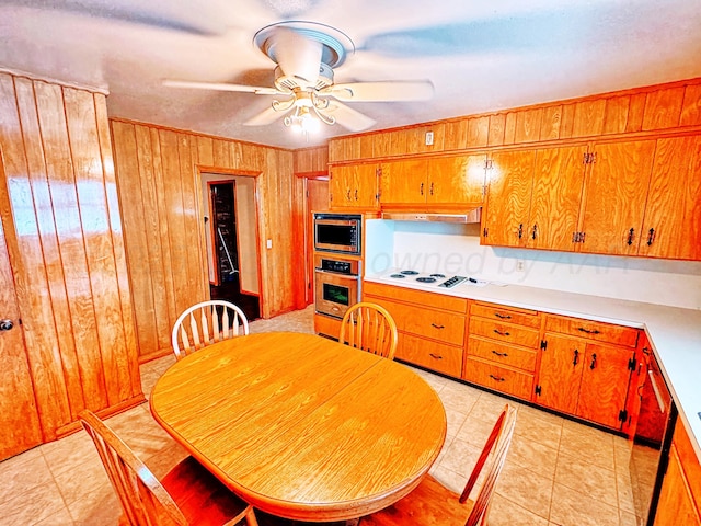 1301 S Fordham St, Perryton, TX 79070 - kitchen featuring built in microwave, oven, wood walls, brown cabinets, and a ceiling fan