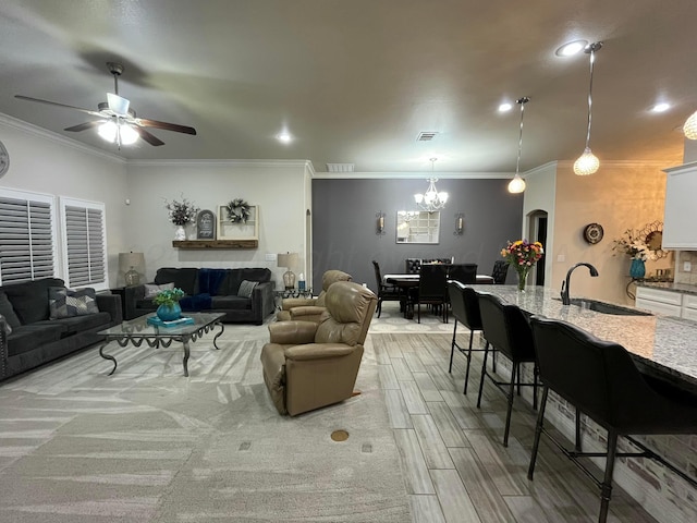 living room with crown molding, light wood-type flooring, visible vents, and ceiling fan with notable chandelier