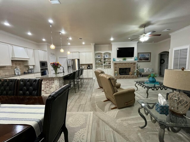 living area with a brick fireplace, a ceiling fan, light wood-style flooring, ornamental molding, and arched walkways