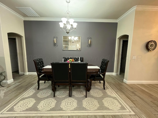 dining area featuring crown molding, visible vents, arched walkways, an inviting chandelier, and light wood finished floors