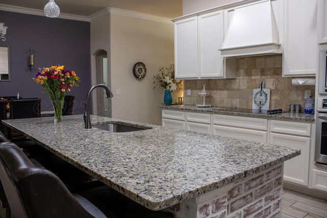 kitchen with light stone counters, a sink, premium range hood, black electric cooktop, and backsplash