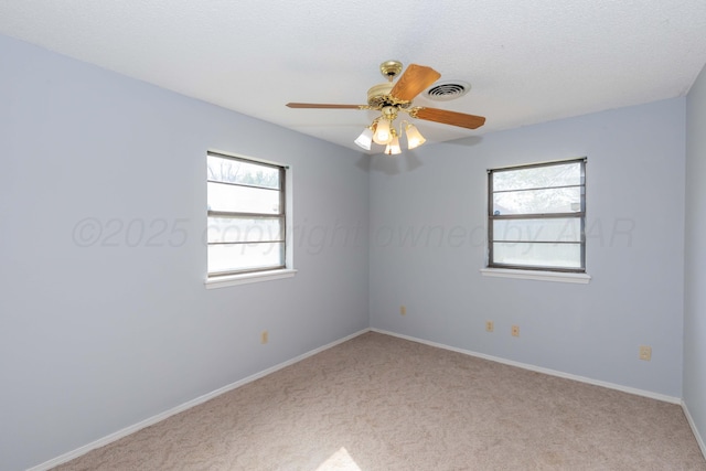 carpeted spare room with ceiling fan, baseboards, visible vents, and plenty of natural light