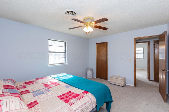 bedroom featuring light carpet, visible vents, a textured ceiling, and ceiling fan