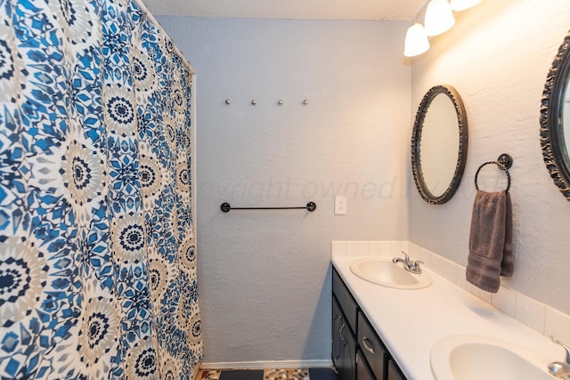 bathroom featuring curtained shower, double vanity, baseboards, and a sink