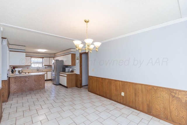 kitchen featuring a sink, wainscoting, open floor plan, freestanding refrigerator, and a chandelier