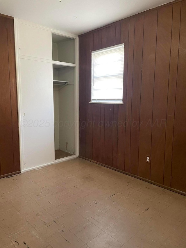 unfurnished bedroom with light floors, wood walls, and a closet