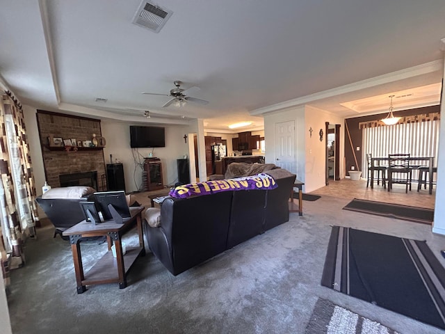 living room featuring carpet, crown molding, a fireplace, a raised ceiling, and ceiling fan