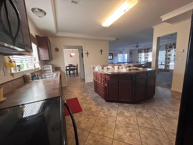 kitchen with a textured ceiling, dark brown cabinetry, sink, ceiling fan, and a center island