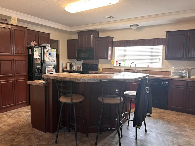 kitchen featuring crown molding, black appliances, a breakfast bar area, and a kitchen island