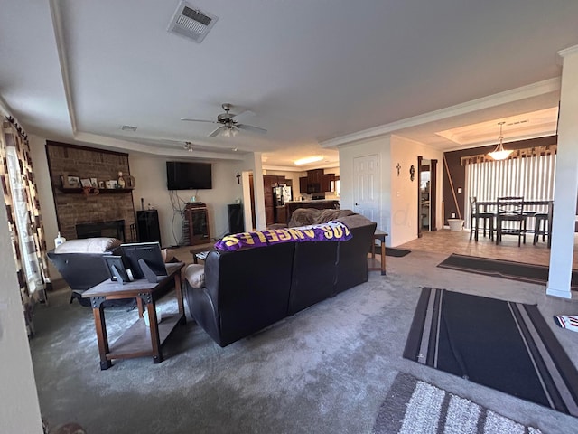 living room featuring a brick fireplace, carpet floors, ceiling fan, and crown molding