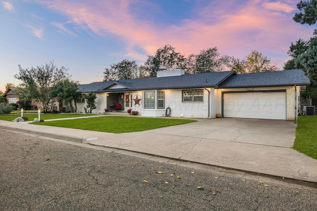 ranch-style home with a lawn, central AC unit, and a garage