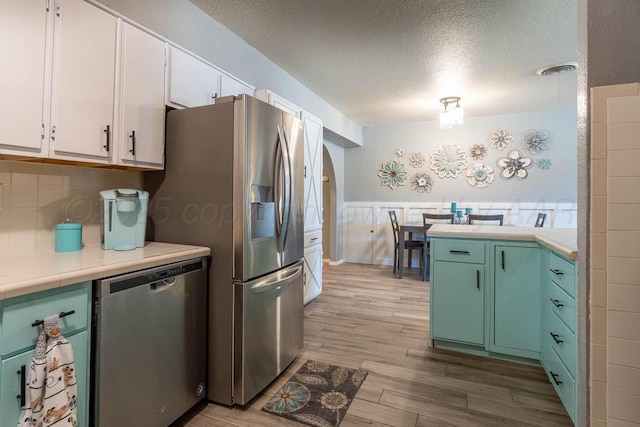 215 Abilene St, Borger, TX 79007 - kitchen with stainless steel appliances, white cabinetry, a textured ceiling, wood finished floors, and backsplash