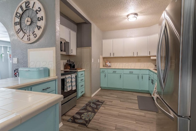 215 Abilene St, Borger, TX 79007 - kitchen with appliances with stainless steel finishes, a textured ceiling, tile counters, light wood-style floors, and white cabinetry