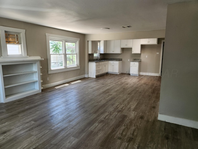 kitchen with baseboards, white cabinets, dark wood-type flooring, and a sink