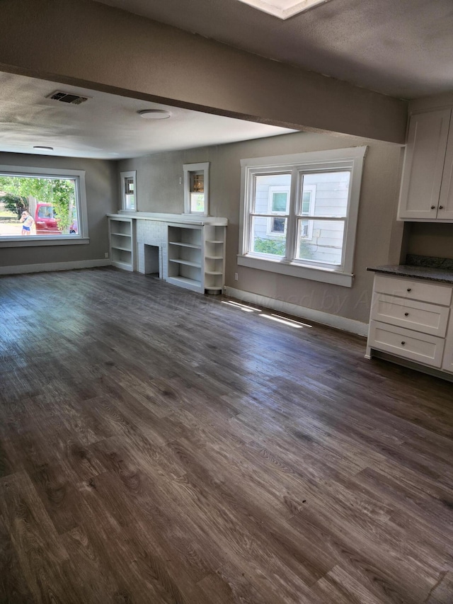 unfurnished living room with dark wood finished floors, healthy amount of natural light, and baseboards