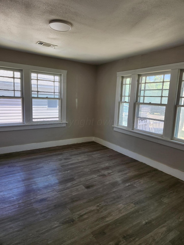 unfurnished room with a textured ceiling, baseboards, healthy amount of natural light, and dark wood-type flooring