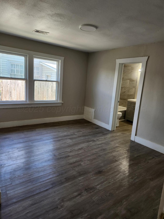 spare room with a textured ceiling, baseboards, and dark wood-style floors