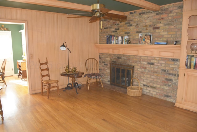 unfurnished living room with wooden walls, ceiling fan, wood finished floors, a brick fireplace, and beam ceiling