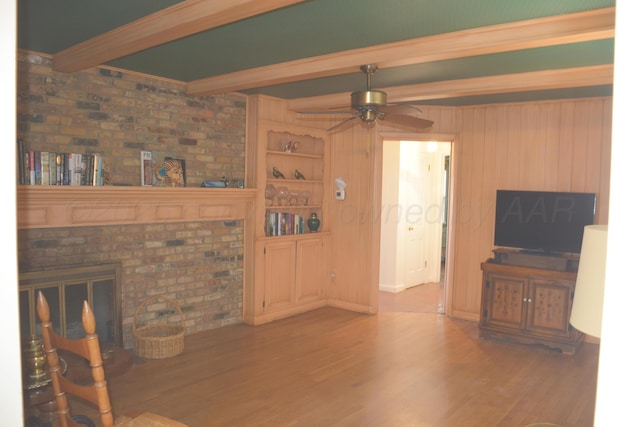 living room with ceiling fan, beamed ceiling, wood finished floors, crown molding, and a fireplace