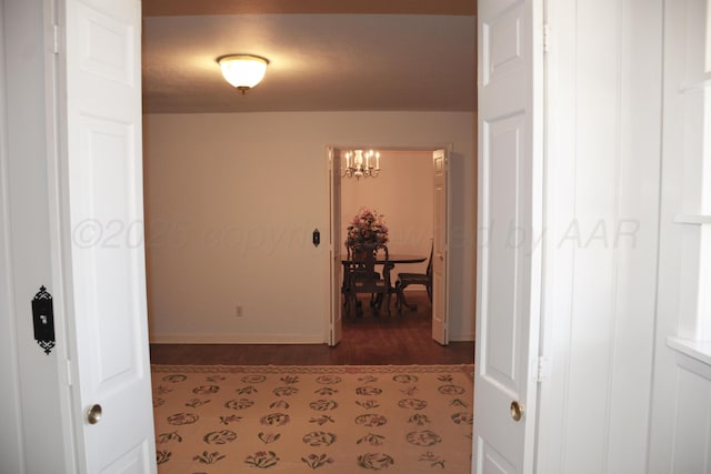 hall featuring dark wood-type flooring, a notable chandelier, and baseboards