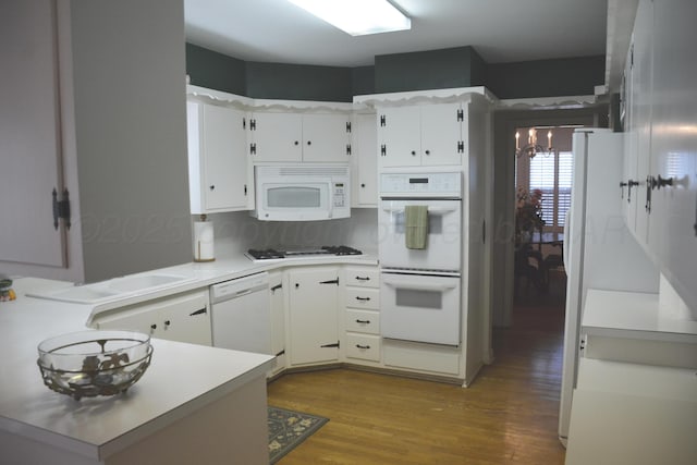 kitchen featuring light countertops, an inviting chandelier, white cabinetry, wood finished floors, and white appliances