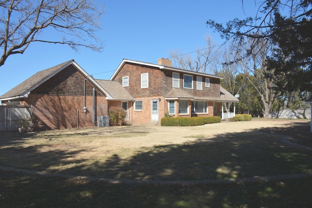 rear view of property with central AC unit, a chimney, fence, a yard, and brick siding