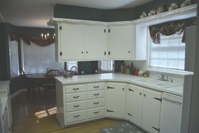 kitchen with white dishwasher, wood finished floors, a sink, white cabinetry, and light countertops