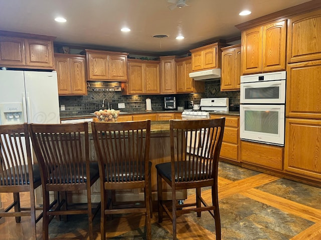 14680 County Road 6, Booker, TX 79005 - kitchen with under cabinet range hood, white appliances, a sink, tasteful backsplash, and a breakfast bar area