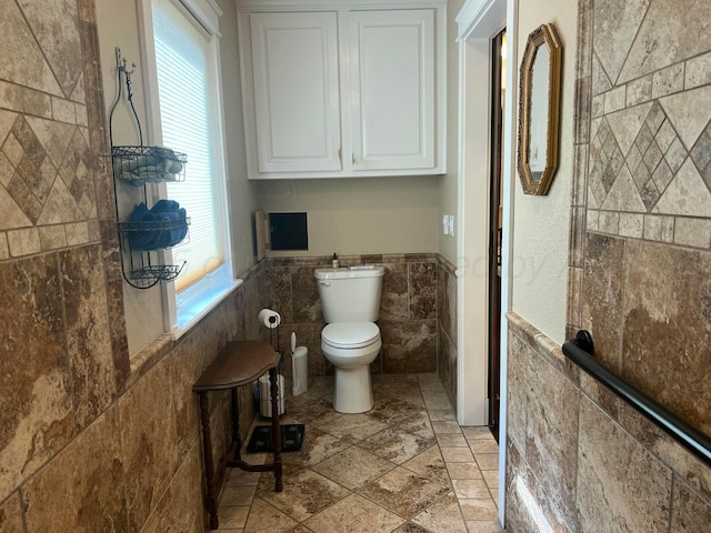 14680 County Road 6, Booker, TX 79005 - bathroom with tile walls, toilet, a wainscoted wall, and stone tile flooring