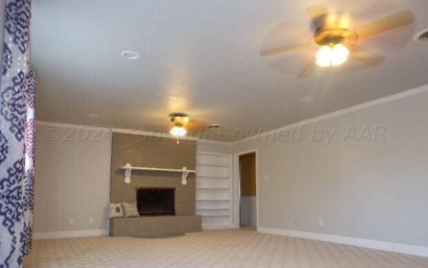 unfurnished living room with built in features, crown molding, carpet flooring, a brick fireplace, and ceiling fan