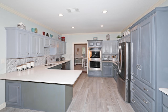 kitchen featuring sink, backsplash, kitchen peninsula, appliances with stainless steel finishes, and ornamental molding