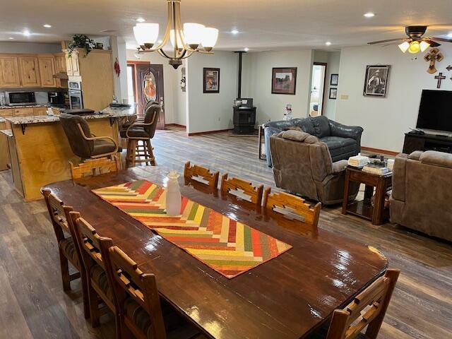 dining room with dark hardwood / wood-style floors, ceiling fan with notable chandelier, and a wood stove