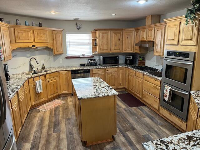 kitchen with sink, stainless steel appliances, dark hardwood / wood-style floors, a center island, and light stone countertops