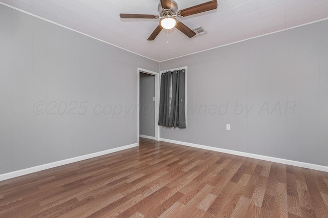 unfurnished room with ceiling fan, wood finished floors, visible vents, baseboards, and ornamental molding