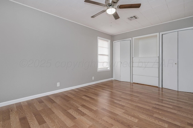 unfurnished bedroom featuring multiple closets, visible vents, ornamental molding, wood finished floors, and baseboards