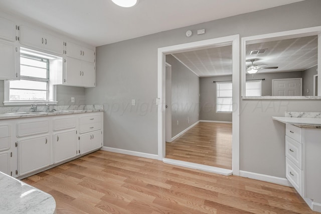 kitchen featuring white cabinets, light wood-type flooring, light countertops, and a sink