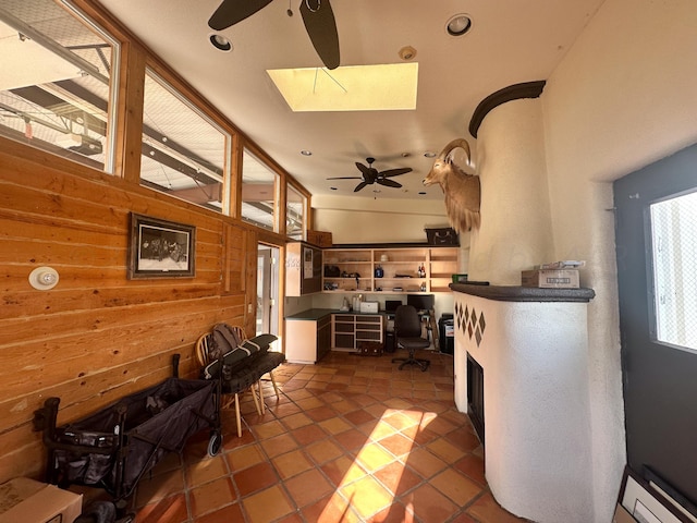 kitchen with dark tile patterned floors, a skylight, wooden walls, and ceiling fan