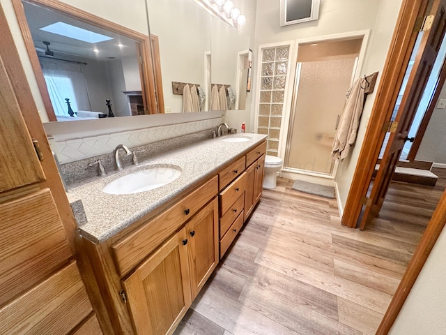 bathroom with wood-type flooring, toilet, a shower with door, vanity, and a skylight